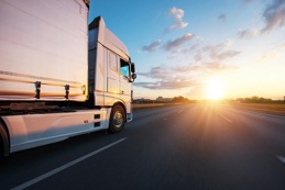 A white HGV driving along a motorway towards a sunny horizon