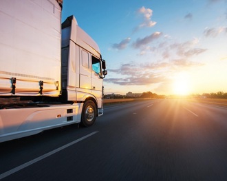 A white HGV driving along a motorway towards a sunny horizon