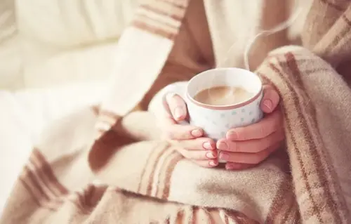  Close-up of hands wrapped in a blanket holding a steaming cup of tea for warmth