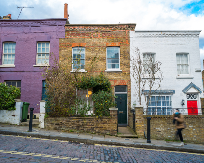 Colorful pastel terraced houses with sash windows, potted plants, and black railings on a charming residential street.