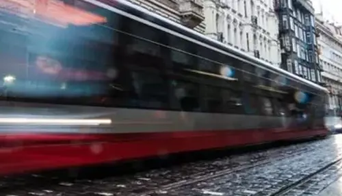 A blurred red and black tram rushes past on a wet cobblestone street in a European city, creating a strong sense of motion.