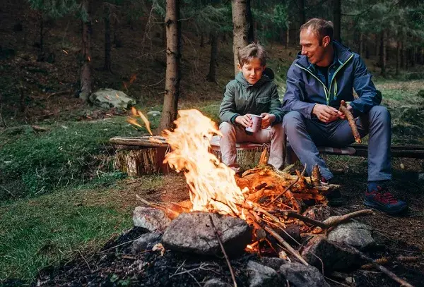 Father and son sitting by a campfire in a forest while camping