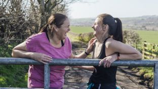 Two women leaning on a metal fence laughing together