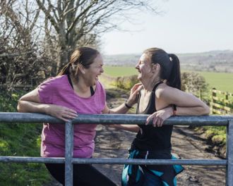 Two women leaning on a metal fence laughing together