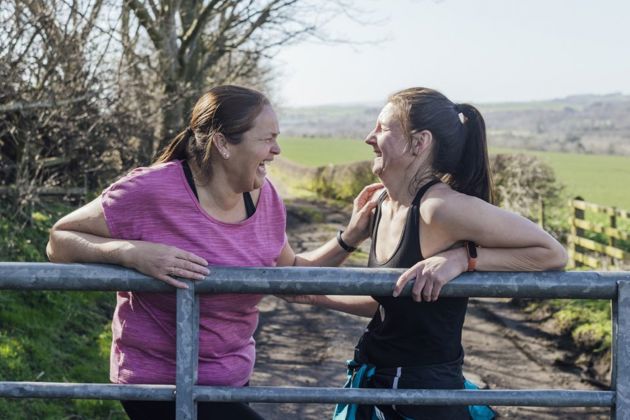Two women leaning on a metal fence laughing together