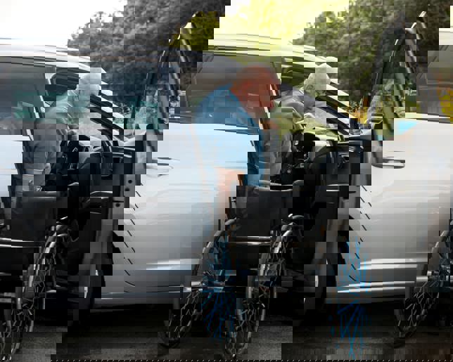 A disabled driver prepares for a day out, moving from his adapted car to his wheelchair on a bright summer morning.