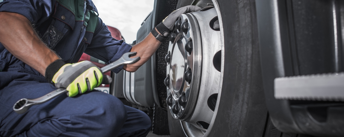 Mechanic in safety gear crouching beside a semi-truck, tightening wheel lug nuts with a large wrench