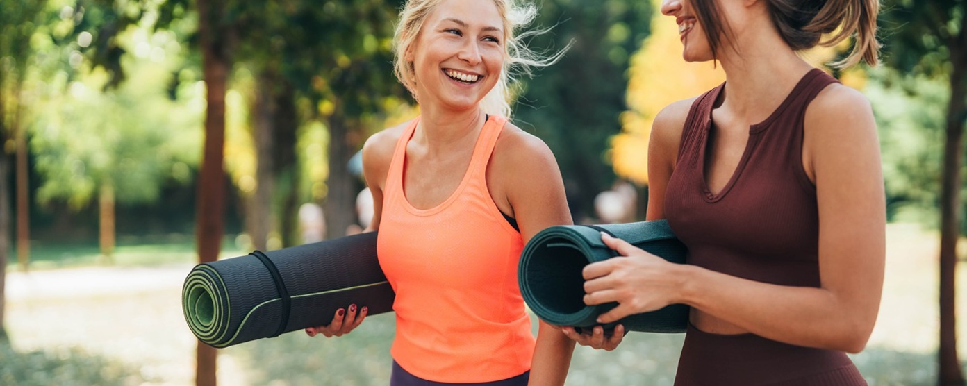 Two young women walking with yoga mats and smiling