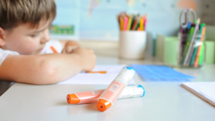 Two epinephrine auto-injectors on a school desk with a child studying in the background, highlighting allergy preparedness