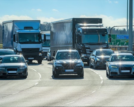 A highway scene showing heavy traffic with cars and large trucks, likely at a junction during peak commuting times.