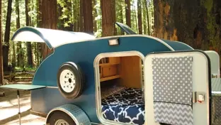 Teardrop camper with open hatch showing renovated interior and bed at a forest campsite