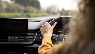 A woman in a yellow jumper driving a car