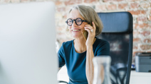 Smiling older women on her mobile phone at computer desk