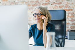 Smiling older women on her mobile phone at computer desk