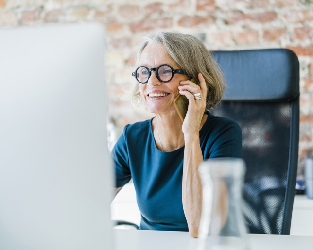 Smiling older women on her mobile phone at computer desk
