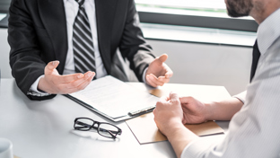 Two men in formal attire discussing documents at a desk.