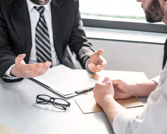 Two men in formal attire discussing documents at a desk.