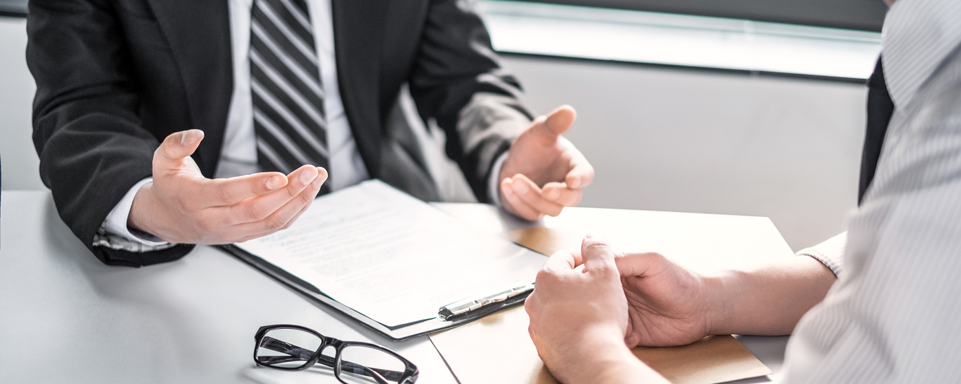 Two men in formal attire discussing documents at a desk.