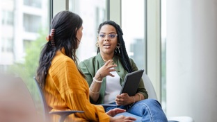 Two professional ladies sit in a medical environment chatting