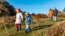 Happy family walking in the countryside. Mother and father with daughter and son on a path through the grass 