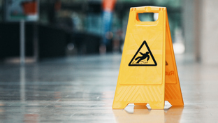 A bright yellow, plastic caution sign is placed on a shiny, reflective floor in an indoor public space.