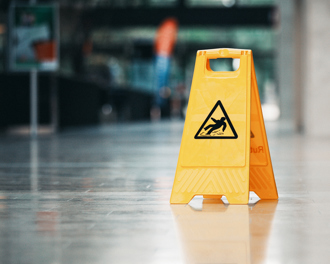 A bright yellow, plastic caution sign is placed on a shiny, reflective floor in an indoor public space.
