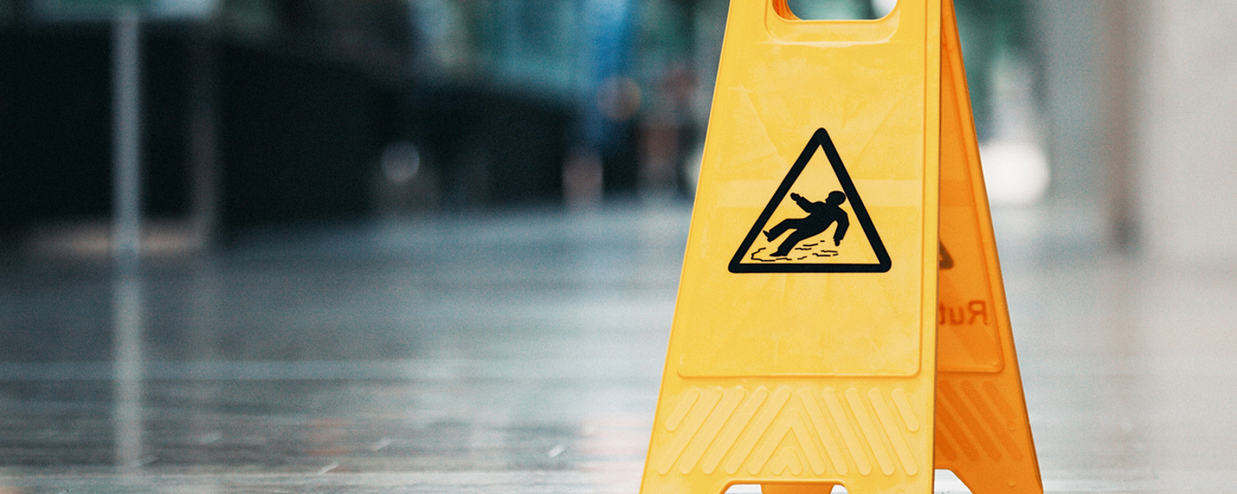 A bright yellow, plastic caution sign is placed on a shiny, reflective floor in an indoor public space.