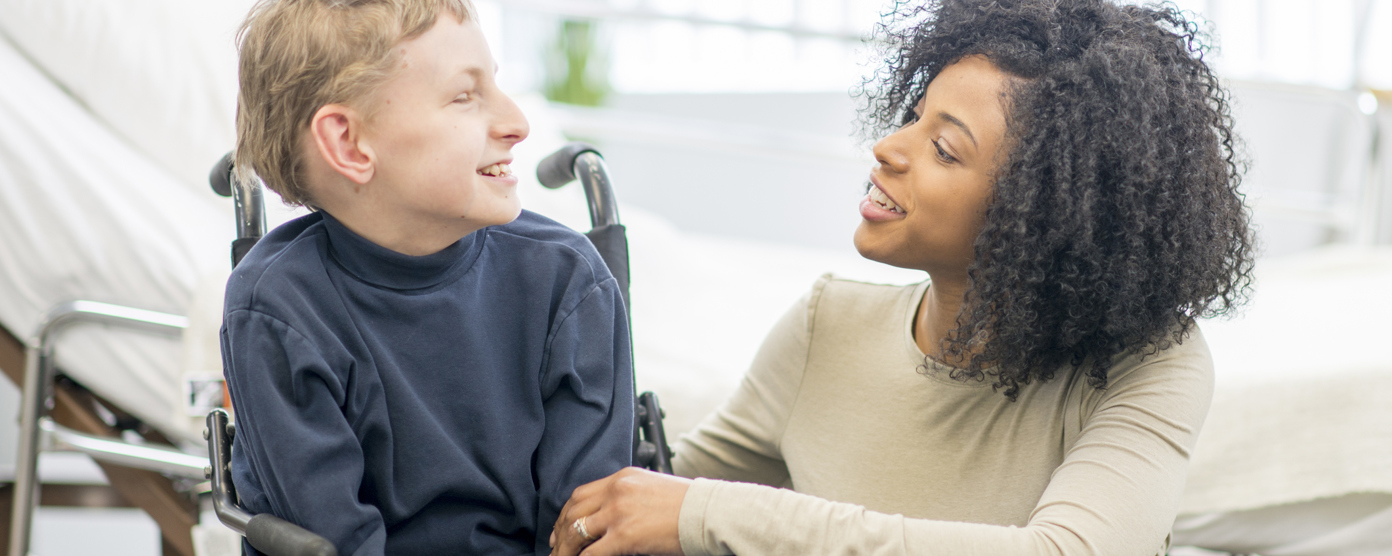 Caring woman in a wheelchair chatting warmly with a smiling boy in a wheelchair in a bright room, offering support and encouragement