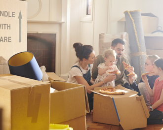 A family enjoys pizza amid moving boxes, sharing a warm moment while settling into their new home.