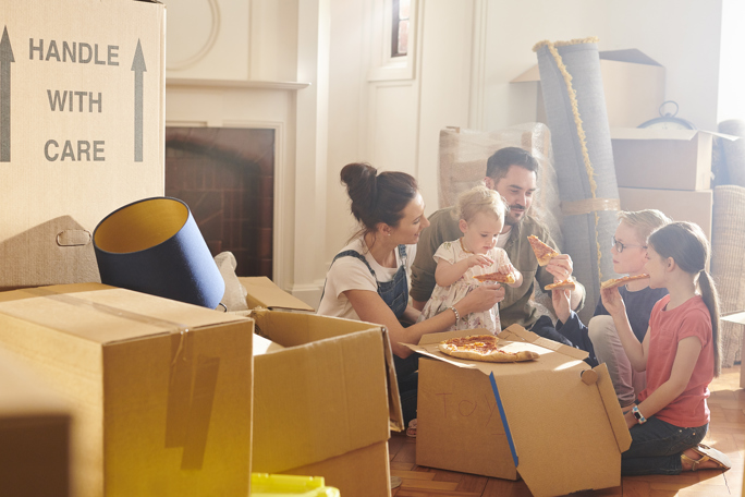 A family enjoys pizza amid moving boxes, sharing a warm moment while settling into their new home.
