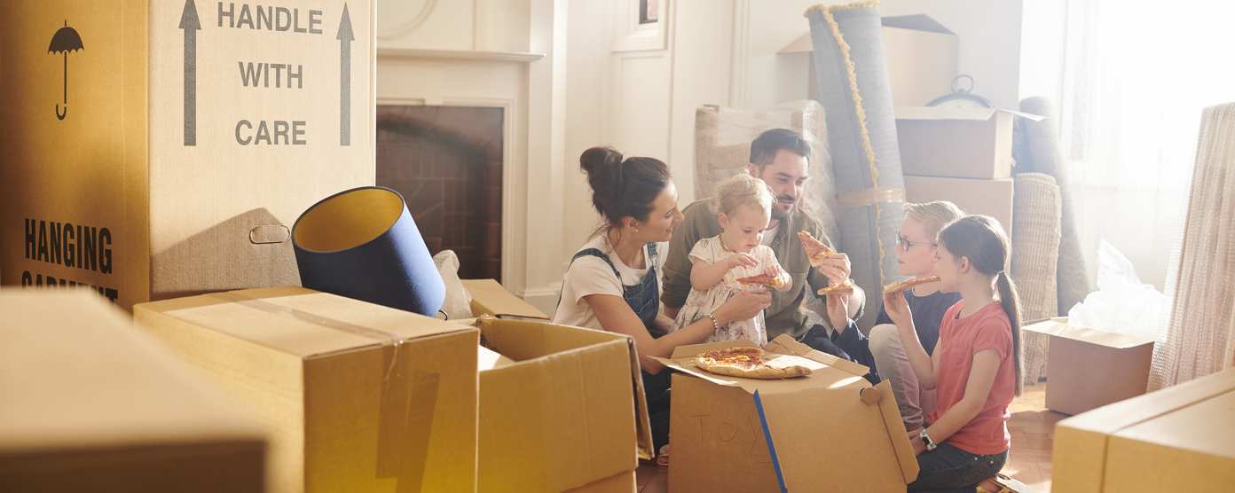 A family enjoys pizza amid moving boxes, sharing a warm moment while settling into their new home.