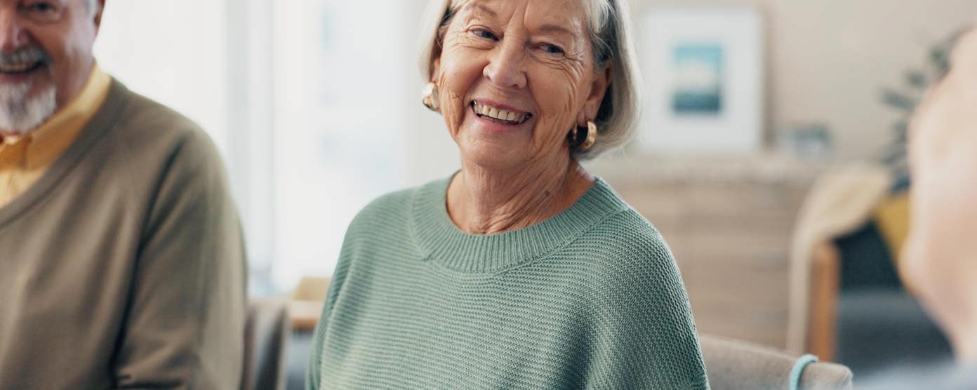 Two elderly residents smiling in a care home living room. 