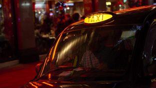 Black cab with lit taxi sign outside a neon‑lit restaurant at night in London