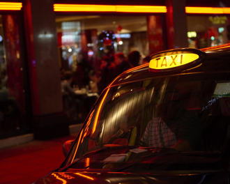Black cab with lit taxi sign outside a neon‑lit restaurant at night in London