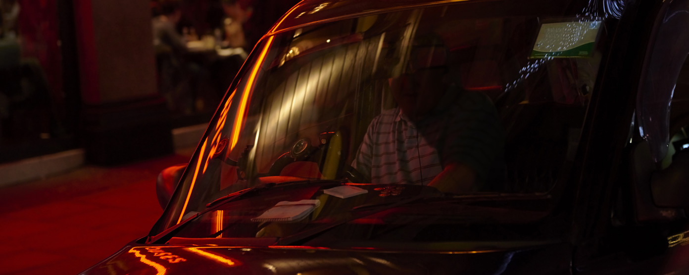 Black cab with lit taxi sign outside a neon‑lit restaurant at night in London