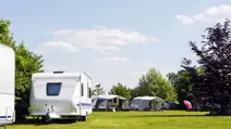 Sunny campsite with caravans and awnings on a wide green lawn under a blue sky with scattered clouds.