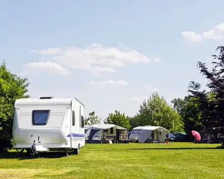 Sunny campsite with caravans and awnings on a wide green lawn under a blue sky with scattered clouds.