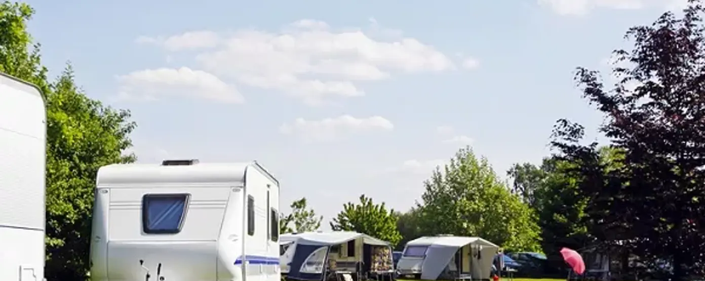 Sunny campsite with caravans and awnings on a wide green lawn under a blue sky with scattered clouds.