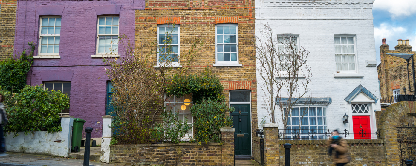 A row of colorful terraced houses, with one painted purple, one left in exposed brick, and another painted white with a bright red door.