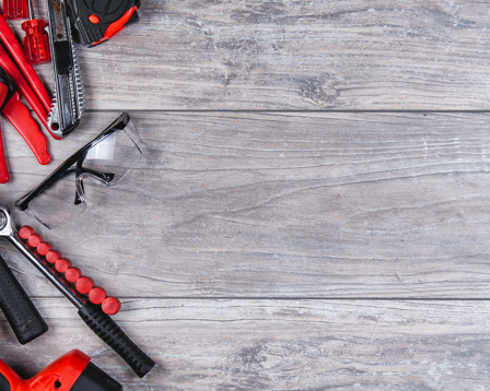 Assorted DIY tools including a drill, hammer and screwdrivers on a wooden workbench with copy space