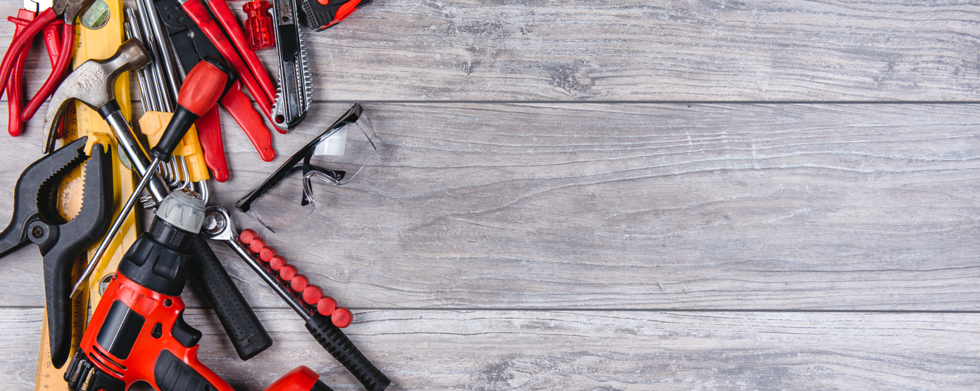 Assorted DIY tools including a drill, hammer and screwdrivers on a wooden workbench with copy space