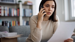 A woman sitting at home on the phone while holding paperwork