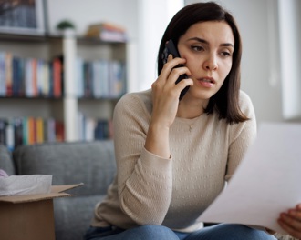 A woman sitting at home on the phone while holding paperwork