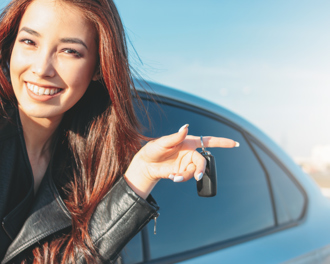 Smiling young woman holding car keys while standing next to a car on a sunny day