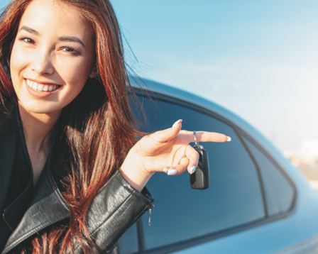 Smiling young woman holding car keys while standing next to a car on a sunny day