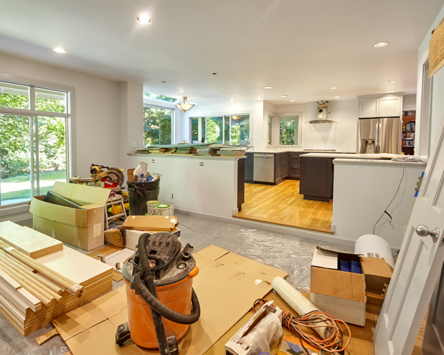Home interior under renovation with construction materials, an orange Shop-Vac vacuum, and partially completed kitchen and living spaces.