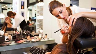 A female makeup artist applying makeup to a brunette in a chair