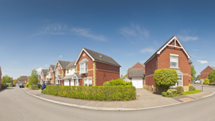 A quiet neighborhood street showcasing modern red-brick houses under a sunny, clear blue sky
