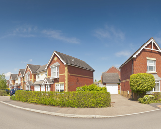 A quiet neighborhood street showcasing modern red-brick houses under a sunny, clear blue sky