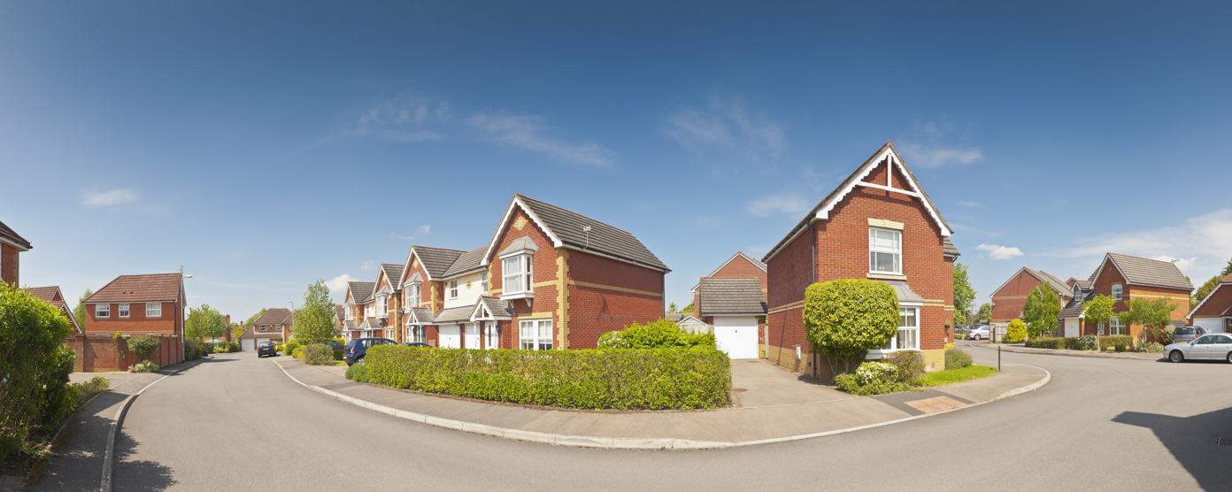 A quiet neighborhood street showcasing modern red-brick houses under a sunny, clear blue sky